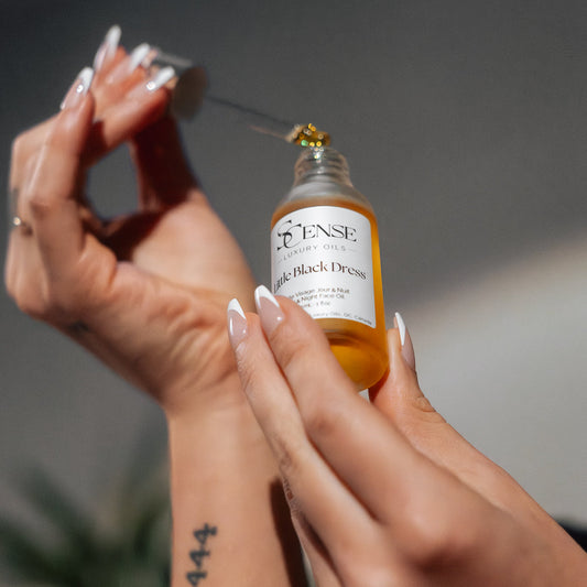 Person holding a dropper glass bottle of Little Black Dress face oil showing the oil in the dropper