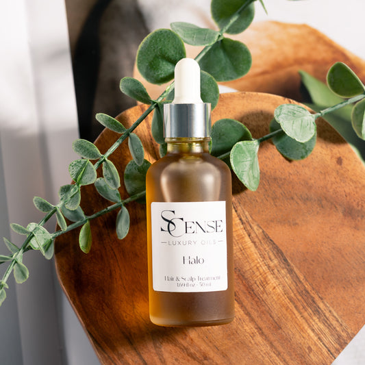 Flat lay of a dropper bottle filled with Halo hair and scalp oil on a wooden tray with Eucalyptus branches