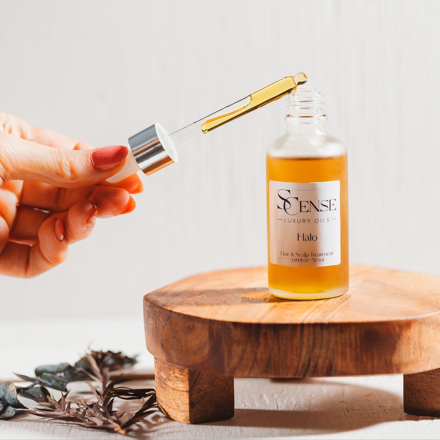 an opened dropper bottle on a wooden tray with a hand holding the dropper showcasing the deep golden oil inside the glass dropper.