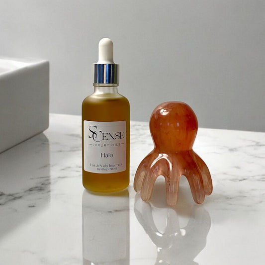 a frosted dropper bottle with Halo hair and scalp oil next to a scalp massager shaped like an octopus made of durable resin on a white marble bathroom counter