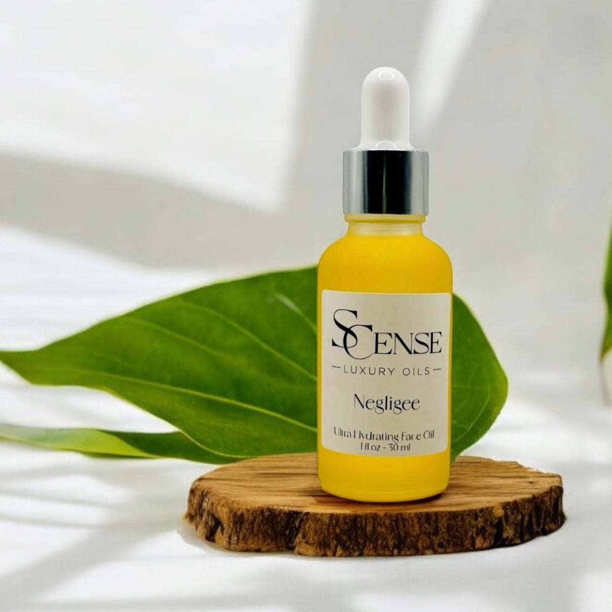 SCense Negligee golden facial oil bottle on a wooden tray with green leaves in soft light