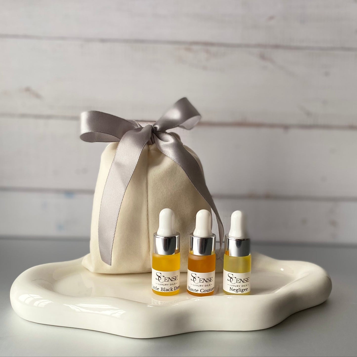 3 mini  testers, 3ml dropper bottles filled with our 3 signature oils on a white tray next to a soft white velvet pouch with a silver ribbon