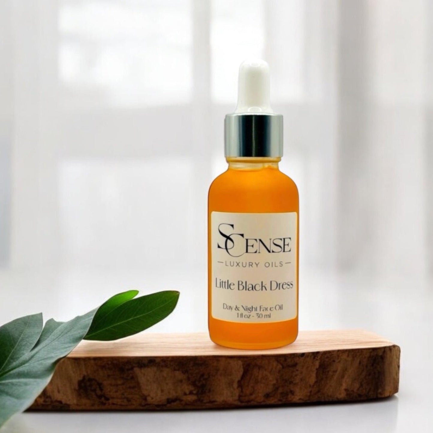 SCense Little Black Dress facial oil bottle in a wooden tray with green leaves in soft natural ligh