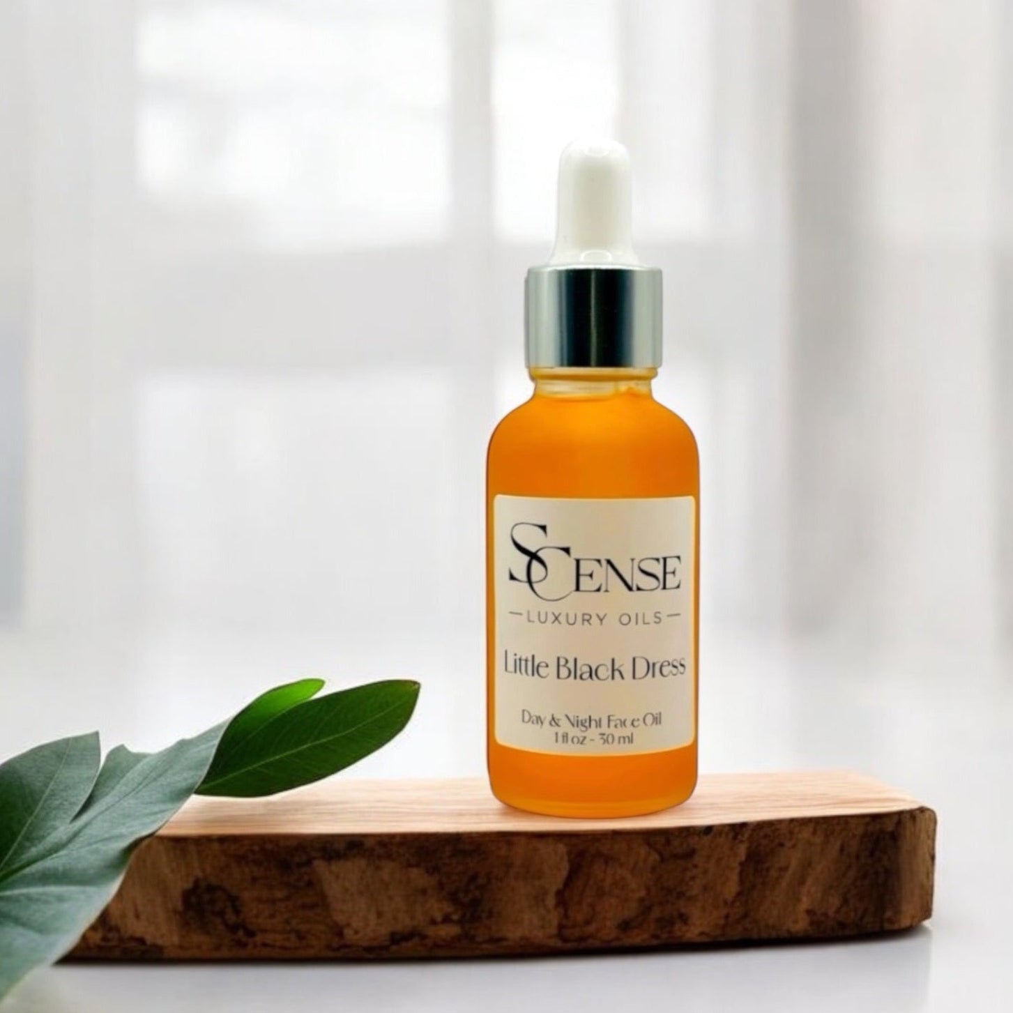 SCense Little Black Dress facial oil bottle in a wooden tray with green leaves in soft natural ligh
